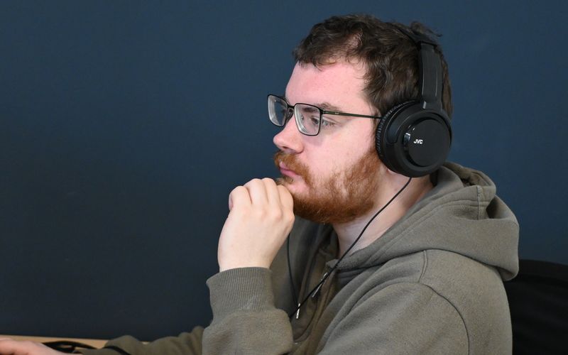 Jonge man met bril en headset werkt geconcentreerd achter een computer.