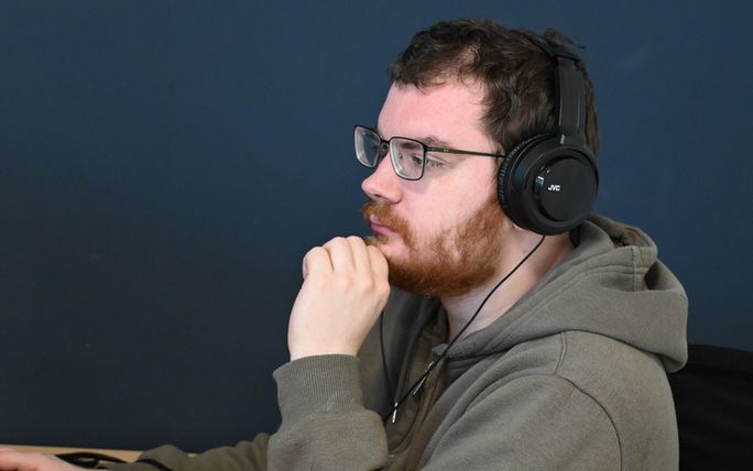 Jonge man met bril en headset werkt geconcentreerd achter een computer.