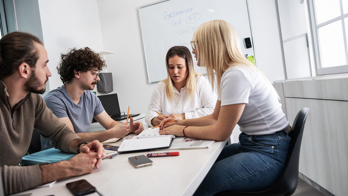 Vier personen overleggen samen aan een tafel met papieren en notitieboeken.