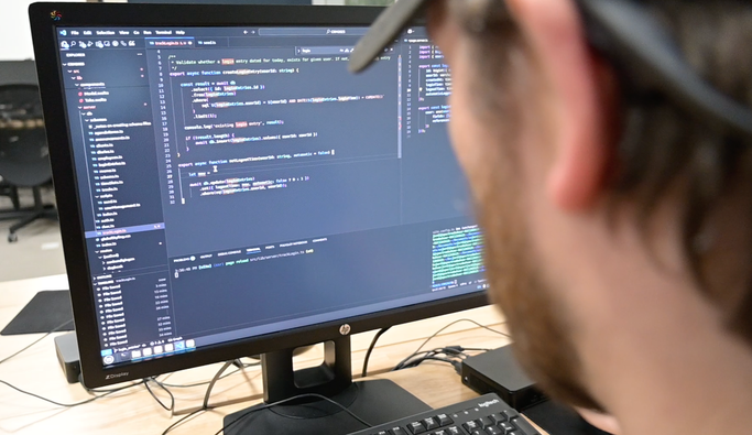 Persoon werkt aan code op meerdere computerschermen in een donkere ruimte.