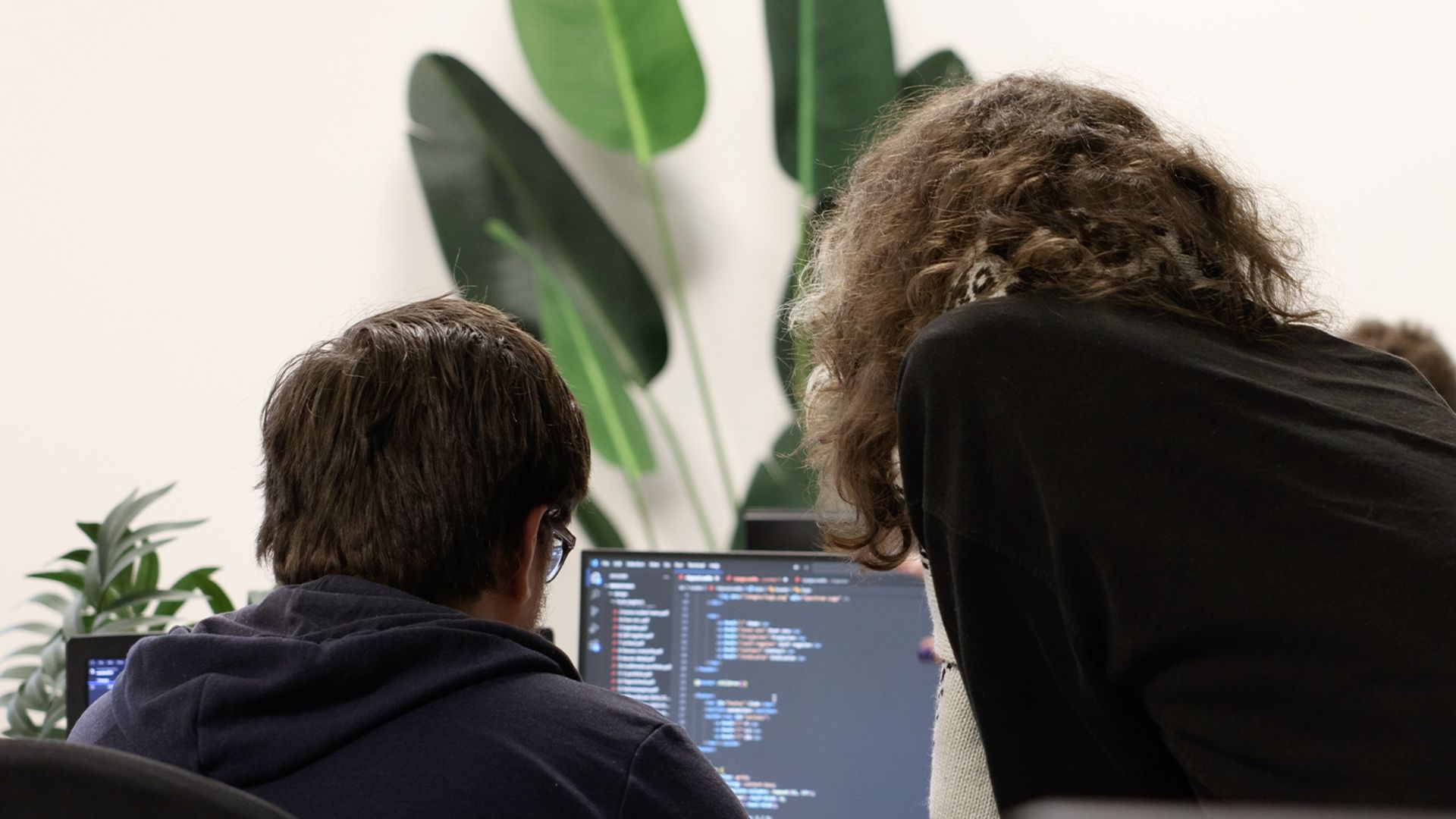 Deelnemer met krullend haar gefotografeerd van achteren in een groepssetting.